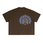 Back of the brown boxy tee with a large blue-and-gold embroidered peacock, tail fanned open, placed off-centre